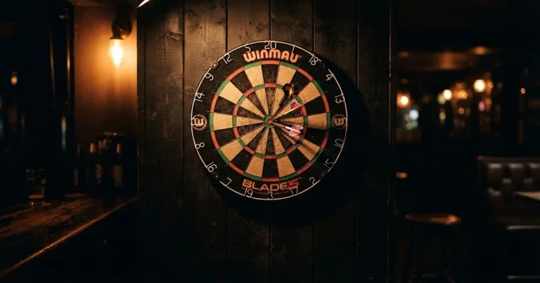 Eine Dartscheibe an einer Holzwand in einem schwach beleuchteten Raum, drei Pfeile stecken nahe der Mitte, warmes Licht von der Seite.